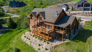 Une grande cabane en rondins à plusieurs étages, dotée d’un balcon imposant, située sur une colline verdoyante, avec une allée menant à l’entrée principale.