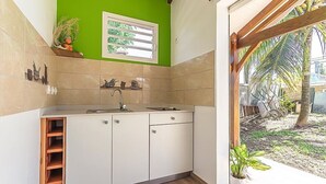 A kitchen with a window, a sink, cabinets, and a potted plant. - Cottage Ramée (Piscine, BBQ, vue sur la mer, montagne, rivière, forêt) (Basse-Terre)