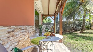 A covered outdoor seating area with a table set for a meal, surrounded by a stone wall and a wooden fence. - Cottage Ramée (Piscine, BBQ, vue sur la mer, montagne, rivière, forêt) (Basse-Terre)