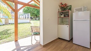 A compact kitchen with a built-in microwave and refrigerator, a wooden ceiling, and a view of a backyard with a patio chair. - Cottage Ramée (Piscine, BBQ, vue sur la mer, montagne, rivière, forêt) (Basse-Terre)