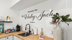 Eine Küche mit weiß gefliestem Fliesenspiegel, einer Holz Arbeitsplatte, einem Spülbecken, einer Vase mit Pflanze und einem Willkommensschild.