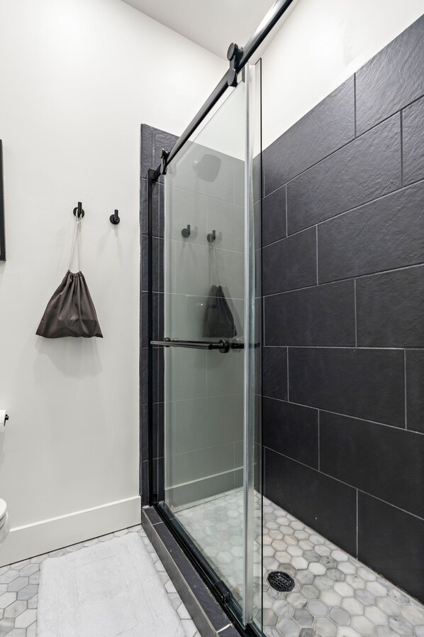 A modern bathroom with a glass shower enclosure, dark tiled walls, and a white floor. - Baylor Loft 4 (Waco)