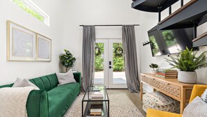 Ein modernes Wohnzimmer mit einem grünen Sofa, einem Couchtisch, einem an der Wand montierten Fernseher und einem großen Fenster mit Vorhängen.