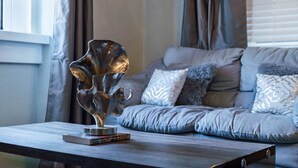 Una sala de estar moderna con un sofá gris, una mesa de centro de vidrio y una escultura decorativa de metal.