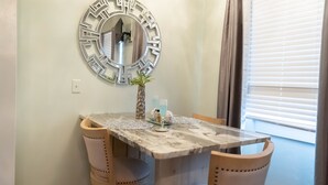 Un comedor con una mesa de mármol, dos sillas, un espejo decorativo y una planta pequeña.