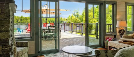 A room with a view of a deck, outdoor furniture, and a stone wall.