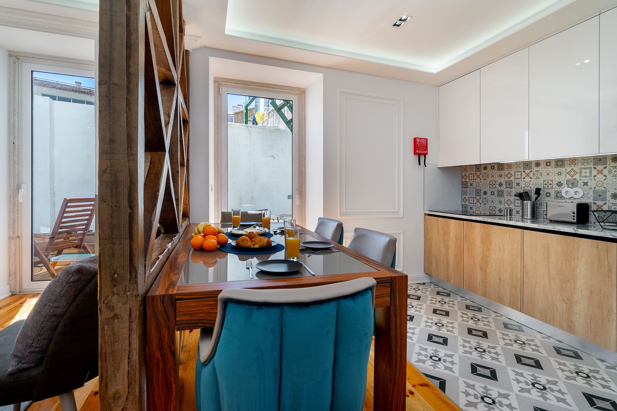 Een moderne eethoek met een glazen tafel, blauwe gestoffeerde stoelen en een ontbijtsetting.