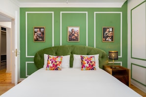 A bedroom with a green wall, a tufted headboard, two floral pillows, and three framed paintings. - Great Location & Family Apartment (Lisbon)