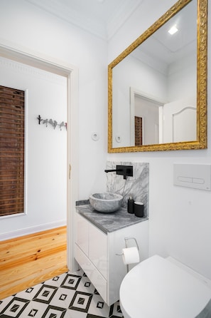 A bathroom with a white toilet, a marble sink, and a gold-framed mirror. - Great Location & Family Apartment (Lisbon)