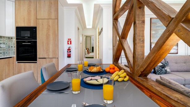 A modern dining area with a wooden table, chairs, and a view of a living room. - Great Location & Family Apartment (Lisbon)