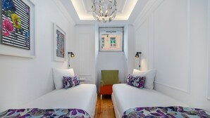 A hotel room with two beds, a green armchair, and a window with a view of buildings. - Great Location & Family Apartment (Lisbon)