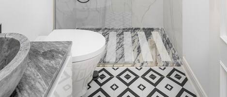 Un baño con ducha de mármol, lavabo con recipiente de mármol y retrete.