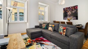 En moderne stue med en grå hjørnesofa, farverigt kunstværk og et spiseområde med et træbord og stole.