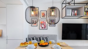 Un espace repas moderne avec une table en bois mise pour le petit-déjeuner, un canapé gris et une bibliothèque remplie de livres.