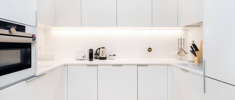 A modern kitchen with white cabinets, a built-in oven, a coffee maker, and a kettle on the countertop.
