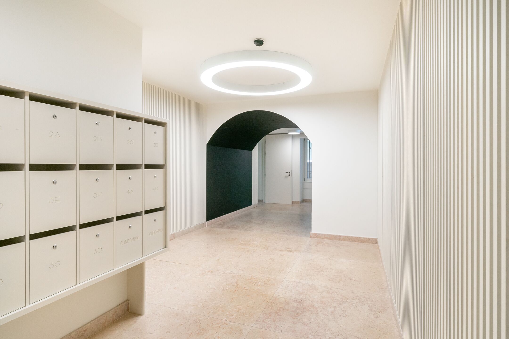 A corridor with lockers, a circular ceiling light, and a green archway.
