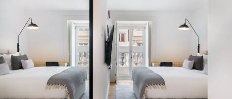 A mirrored view of a bedroom with two beds, a TV, and a balcony with a view of buildings.