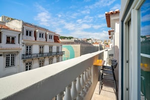 A balcony with a view of historic buildings, a table with chairs, and a glass door. - Prime Location Luxury Apartment (Lisbon)