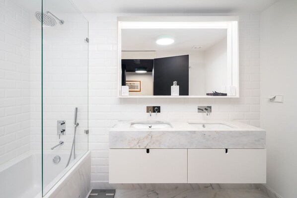Un baño moderno con ducha envuelta en vidrio, un lavabo de mármol blanco y un espejo grande sobre el mueble.
