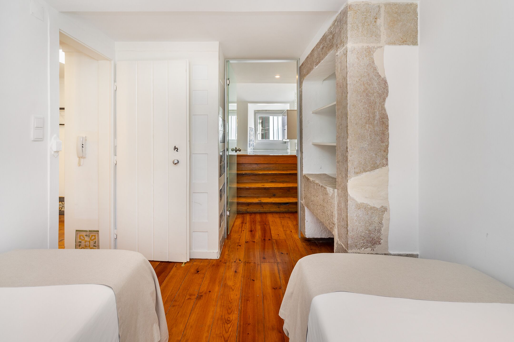 Une chambre avec deux lits, un plancher en bois, une porte blanche et un escalier menant à une autre pièce.