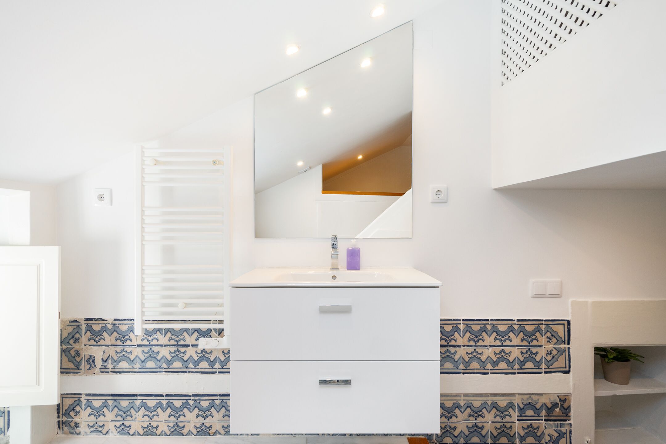 A bathroom with a white vanity, a mirror, and patterned tiles.