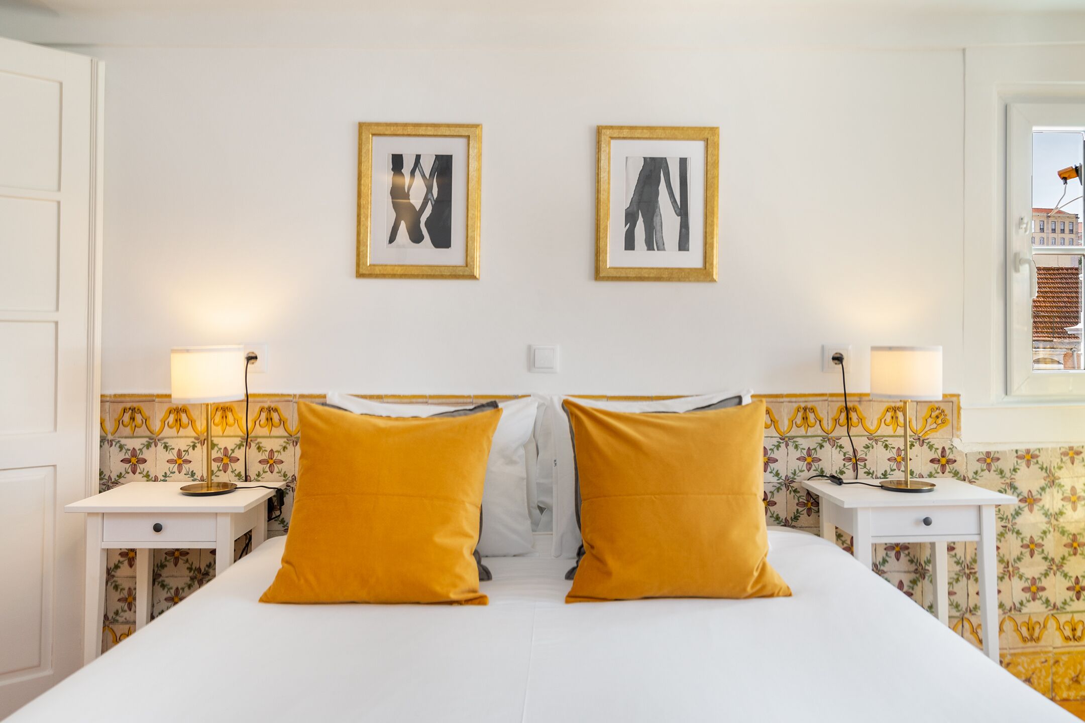 Une chambre d’hôtel avec un lit, deux tables de chevet, deux lampes et deux tableaux encadrés au mur.
