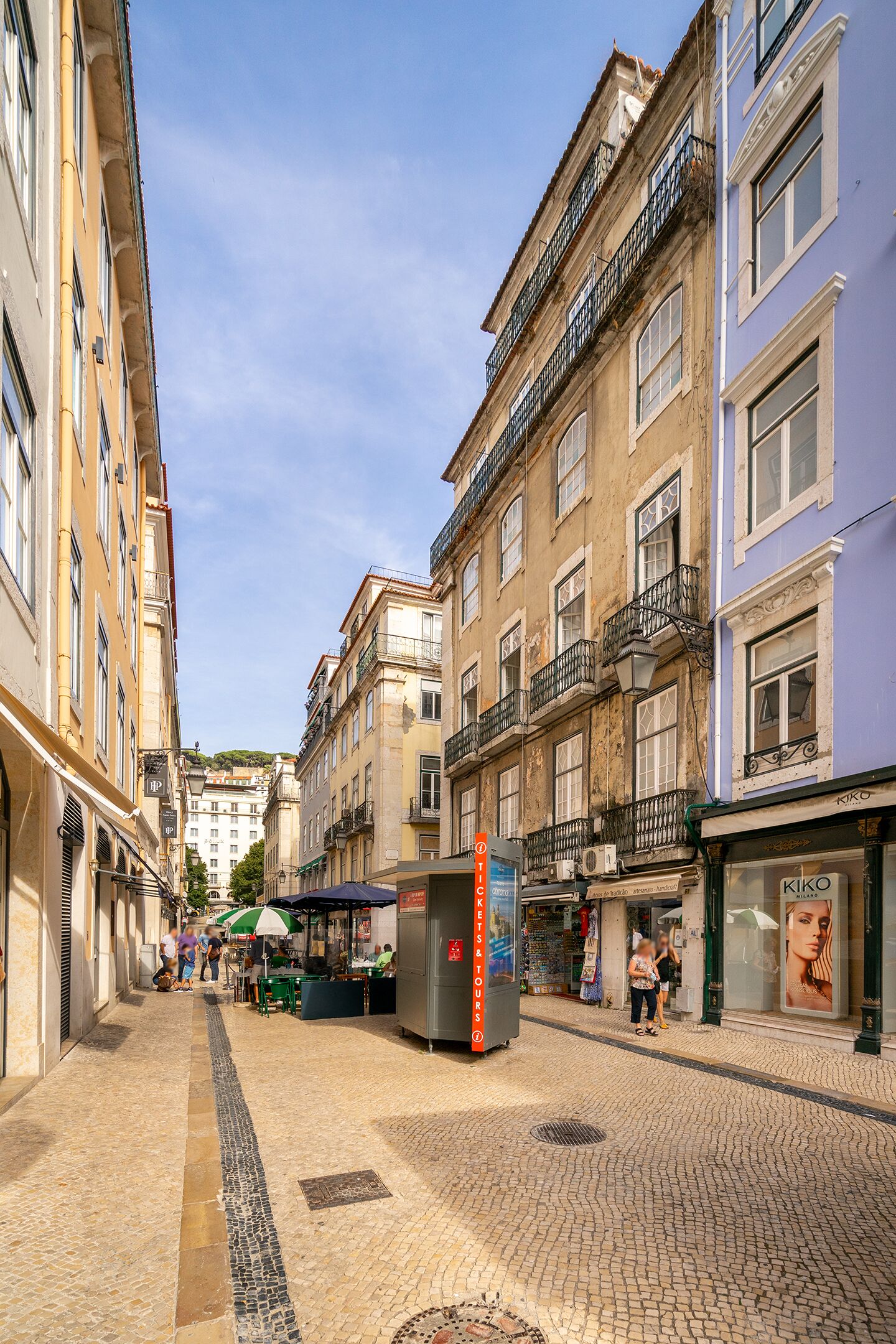 Une rue pavée bordée de bâtiments historiques, un kiosque et un magasin KIKO.