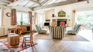 A spacious living room with wooden beams, a fireplace, striped armchairs, and a dining area with a wooden table and chairs. - Le Moulin de Pilet 4* - Proche Puy du Fou (Mortagne-sur-Sèvre)