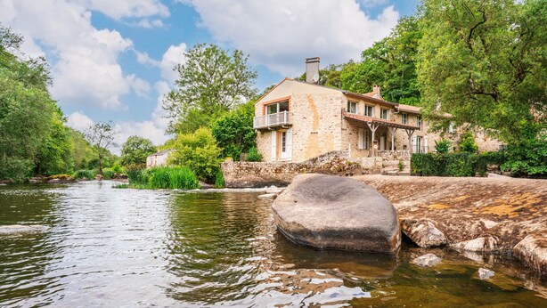 A stone house with a balcony overlooking a river, surrounded by greenery. - Le Moulin de Pilet 4* - Proche Puy du Fou (Mortagne-sur-Sèvre)