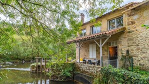 A stone house with a balcony overlooking a calm river, surrounded by lush greenery. - Le Moulin de Pilet 4* - Proche Puy du Fou (Mortagne-sur-Sèvre)