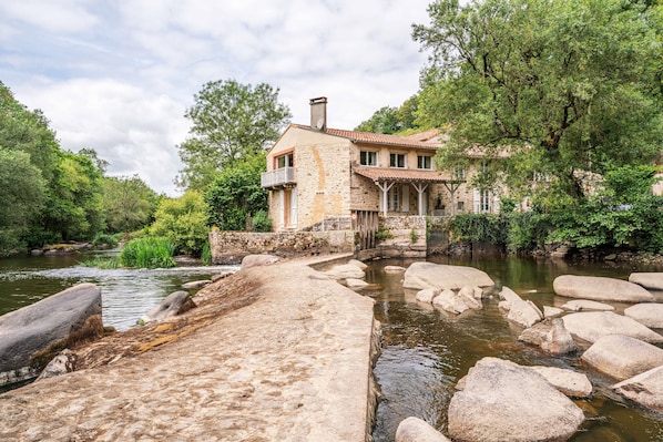 A stone house with a balcony, a river in front, and a stone bridge.