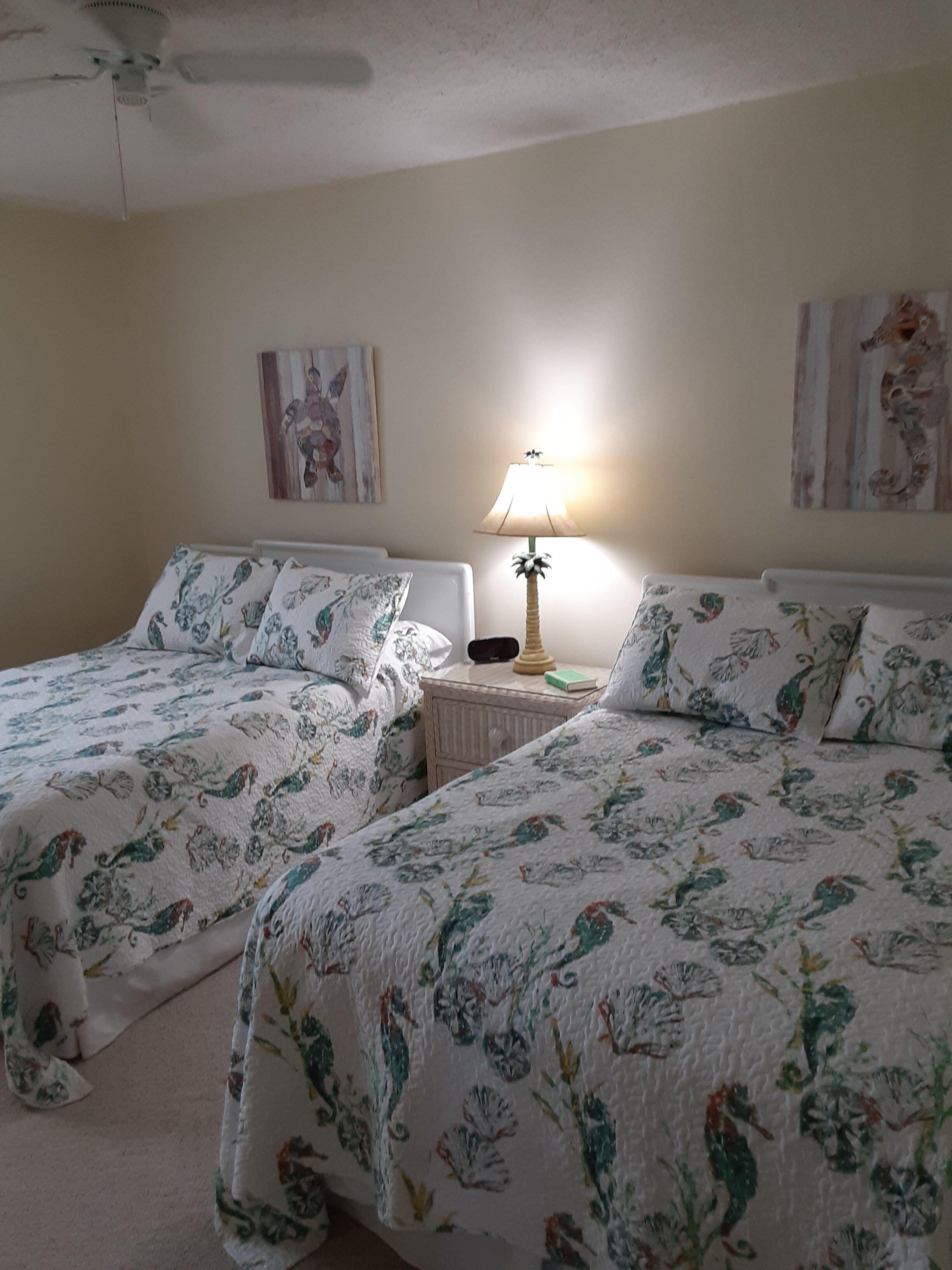A bedroom with two beds, a nightstand, a lamp, and artwork on the walls.
