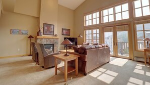 A spacious living room with a fireplace, comfortable seating, and large windows offering a view of the outdoors. - Largest Passage Point Condo with Hot Tub, Vaulted Ceilings, Huge Balcony - PP514 (Copper Mountain)