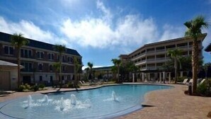 A swimming pool with water fountains, surrounded by a brick walkway and palm trees.