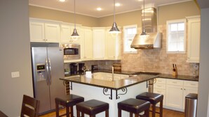 Una cocina moderna con armarios blancos, electrodomésticos de acero inoxidable y una isla central con taburetes de bar.