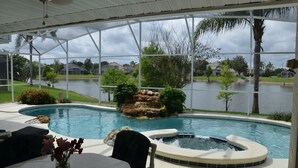 Un espace piscine avec un jacuzzi, une table décorée de fleurs et une vue sur un lac et des maisons.