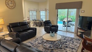 Un salon avec un canapé en cuir noir, une table basse, un téléviseur et un coin repas comprenant une table et des chaises.