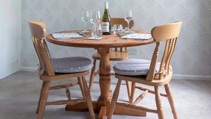 Een ronde houten eettafel met vier stoelen, een fles wijn en verschillende lege wijnfluiten.