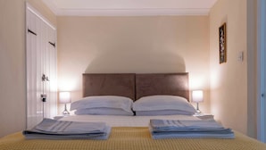 Een hotelkamer met een tweepersoonsbed, twee nachtkastjes met lampen, een deur met slot en een lijst met een afbeelding aan de muur.