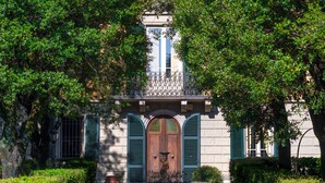 Un bâtiment doté d’une entrée centrale, flanqué de deux portes avec des volets verts, et d’un balcon situé au-dessus.