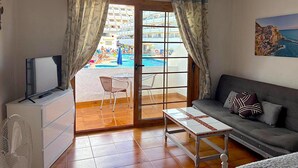 Une pièce comprenant un canapé, une table, un téléviseur et donnant sur une piscine et des bâtiments situés à l’extérieur.