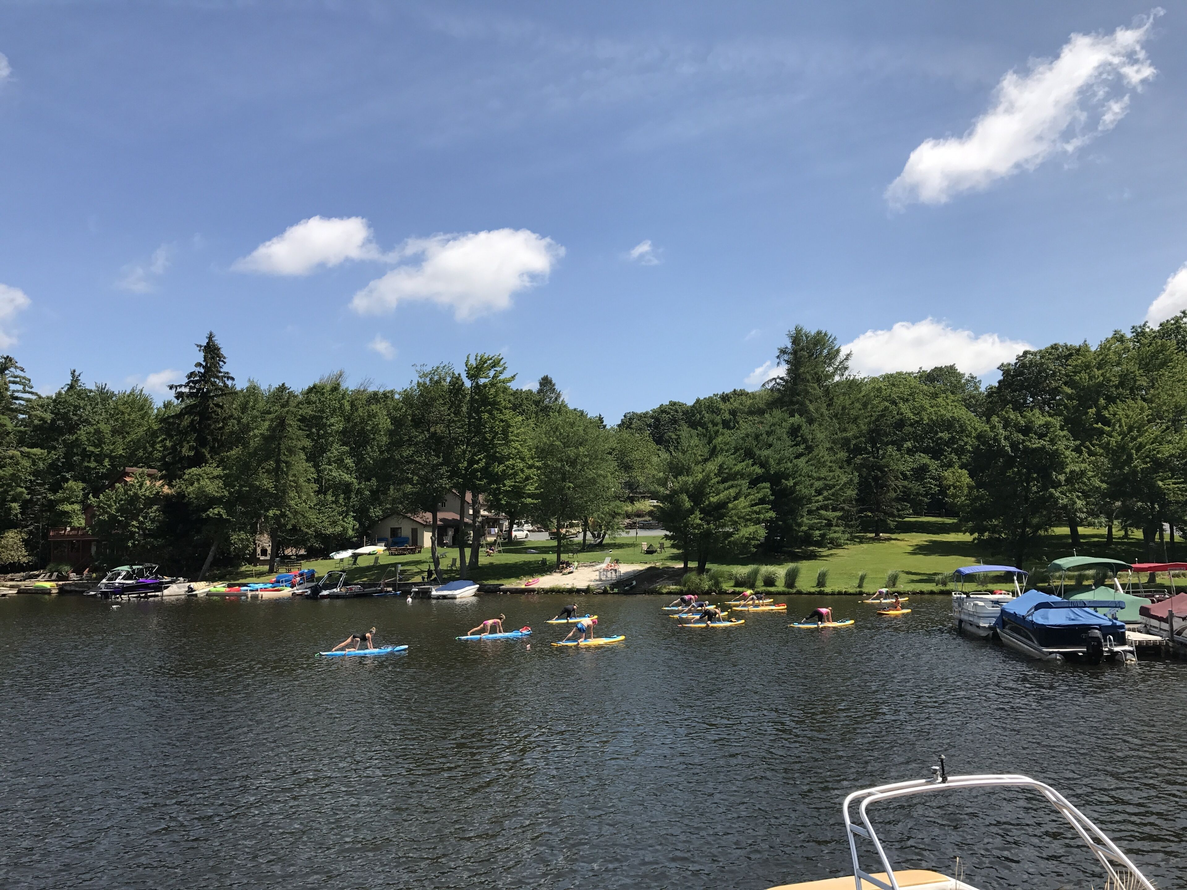 Un lac où l’on voit des bateaux et des personnes sur des planches de surf, entouré d’arbres et bordé d’un terrain de golf.