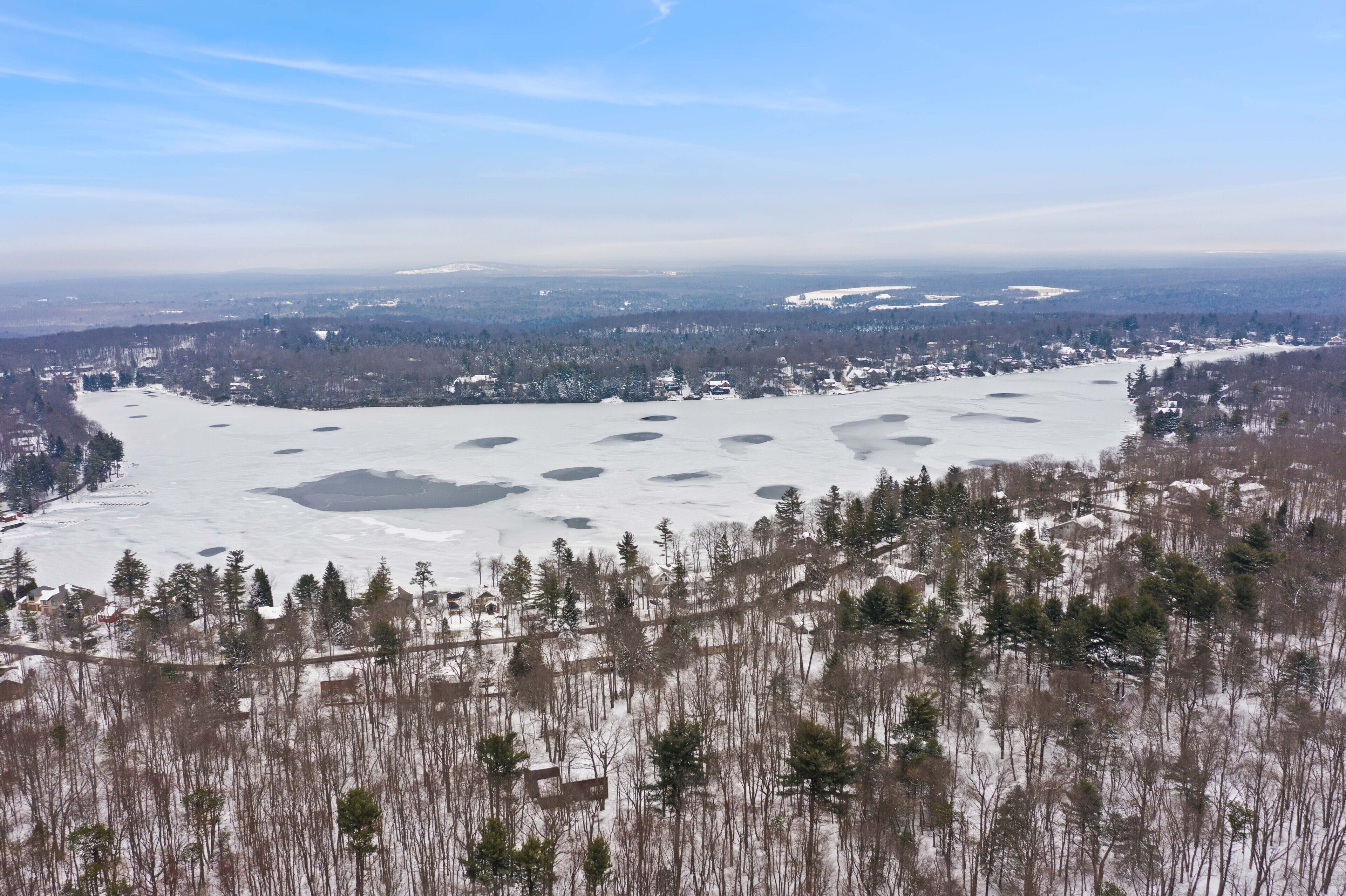 Een panoramisch uitzicht op een winterlandschap, met besneeuwde grond, bomen en een verafgelegen stadsbeeld.