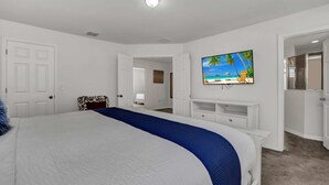 Une chambre à coucher avec un grand lit, un téléviseur fixé au mur et une porte donnant sur une autre pièce.