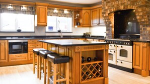 Une cuisine avec des meubles de rangement en bois, un grand îlot central doté de tabourets, un meuble à vin et un four en briques.