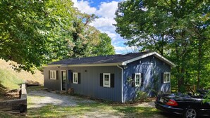 A small, single-story building with a dark blue exterior and white trim. It features a front door, two windows with shutters, and a small porch area. - Claytor Lake Hideaway (Pulaski)