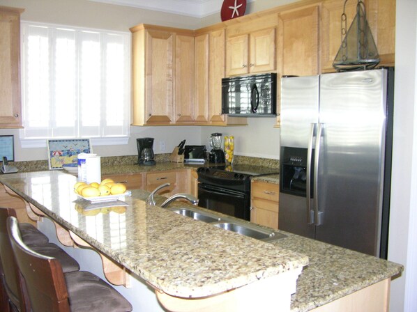 A kitchen with granite countertops, wooden cabinets, stainless steel appliances, and a breakfast bar.