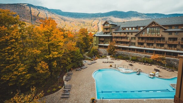 Een resort met een zwembad, ligbedden en een bergachtig achtergrond.