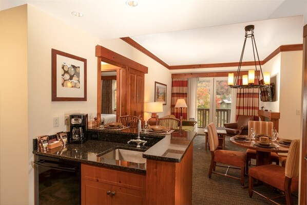 A hotel room with a kitchen area, dining space, and a view of the outdoors. - 2 BR Lodge at Spruce Peak (Stowe)