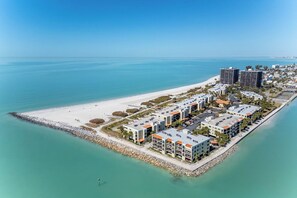 Vista aérea de un complejo turístico frente al mar, con propiedades en primera línea de playa, una playa de arena y un mar azul y claro.